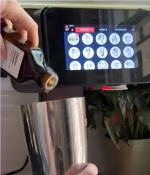 Hand adding Ripples Foamer to a cocktail shaker, next to a cocktail printer